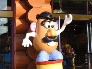 Mr. Potato Head outside a shop in the sunlight waving his arm